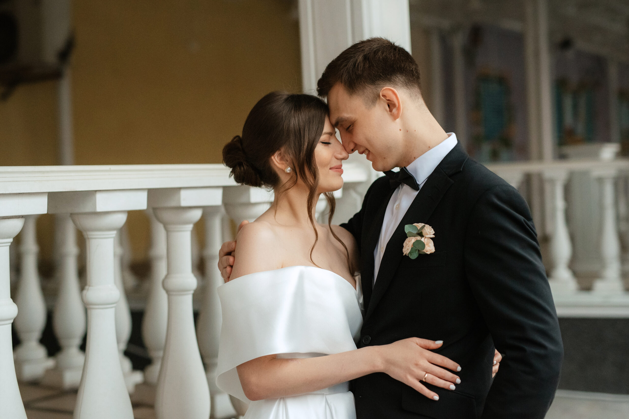 Eine Braut und ein Bräutigam umarmen sich, berühren ihre Stirnen in formeller Hochzeitskleidung in einem Raum, ihr Moment perfekt inszeniert von einer aufmerksamen Hochzeitsplanerin.